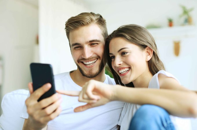 Zwei fröhliche Personen sitzend auf Mobiltelefon schauend